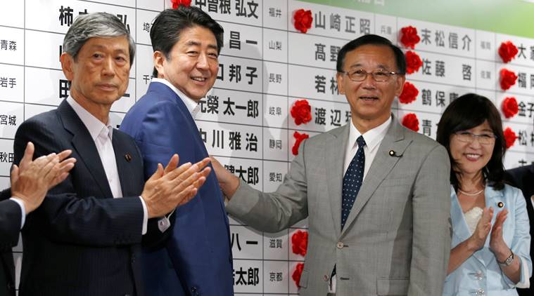 Japan's Prime Minister Shinzo Abe, who is also leader of the ruling Liberal Democratic Party, smiles with party senior members as they put a rosette on the name of a candidate who is expected to win the upper house election in Tokyo, Japan